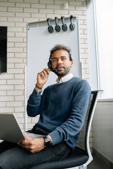 Confident young call center agent working with laptop and headset in a modern office setting.